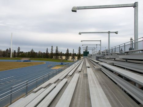 Rows of bleachers at a running track on a cloudy spring day.