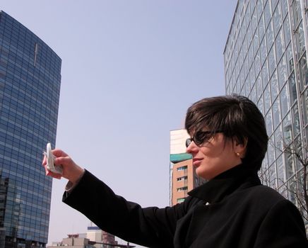  Businesswoman taking images with a cellular phone photocamera in a big city.         