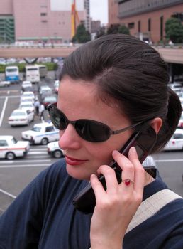 Woman with sunglasses using mobile phone in a big city.          
