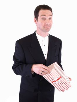 A white male in a suit puts his hand into a popcorn bag. He is chewing on something in his mouth.