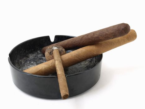Three cigars resting in a dirty ashtray isolated on a white background.