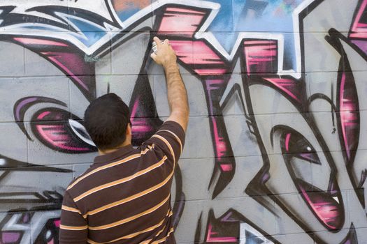 A graffiti artist at work spray painting a brick wall.
