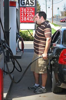 A man pumping high priced gas into his car with a disgusted look on his face.