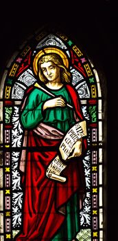 detail of viktorian stained glass church window in Fringford depicting St John the Evangelist, a scroll in his hands with the beginning of his gospel in latin "In principio erat verbum"