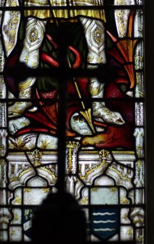 detail of victorian stained glass church window in Fringford depicting St. George killing the dragon, large black cross in foreground, focus on window