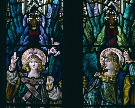 detail of victorian stained glass church window in Fringford depicting two typical victorian angels with a sword and a lily in their hands