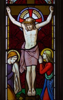 detail of victorian stained glass church window in Fringford depicting Jesus nailed to the cross with St. Mary and St. John at the feet of the cross