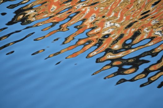 The reflection of a sunlit old orange-bricked building in a blue wavy water surface makes a very abstract pattern for a background image. Alsterfleet in Hamburg.