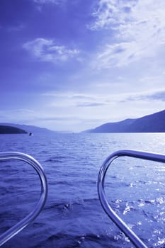 blue waterscape seen from a boat, focus on front waves, railing visible, picture taken on Loch Ness, Scotland, UK