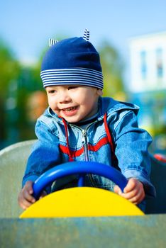 happy three year old boy driving a toy car outdoor in the park