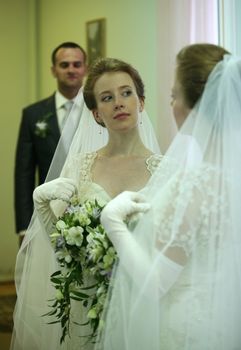 The beautiful young bride and the groom are reflected in a mirror