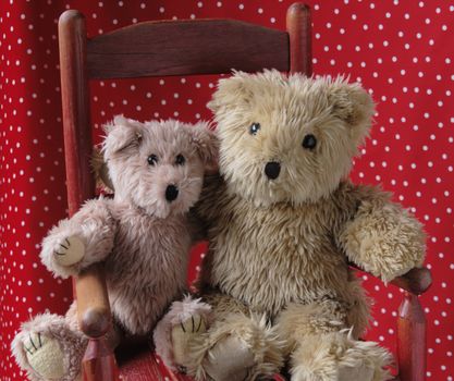 two teddy bears in an old child's red chair with a red and white polka dot background