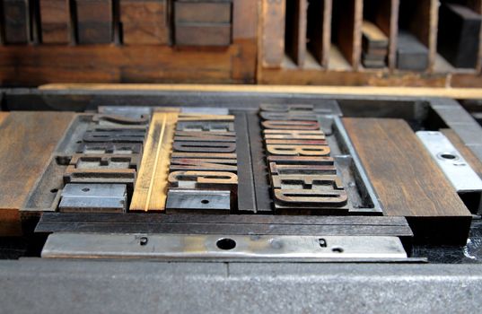 wood type clamped into a printer's chase just before inking, against a background of printer's furniture
