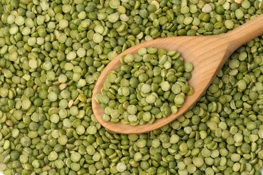 Wooden spoon full of split green peas on legume background