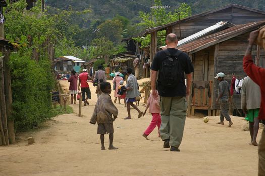 Large tourist man walking among the children in a small town in Madagascar