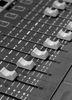 Faders of a studio soundboard.  Black and white image scanned from medium format film. Film grain visible.
