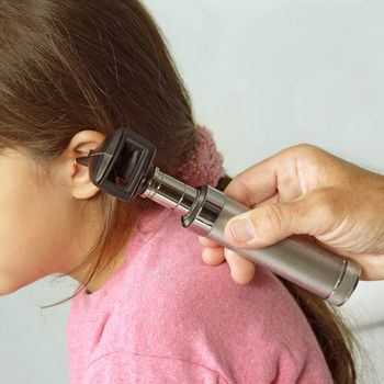 A close-cropped image of a doctor examining the ear of a young girl with a otoscope.
