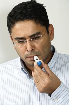 A male in his 30's checking his temperature with a digital thermometer.
