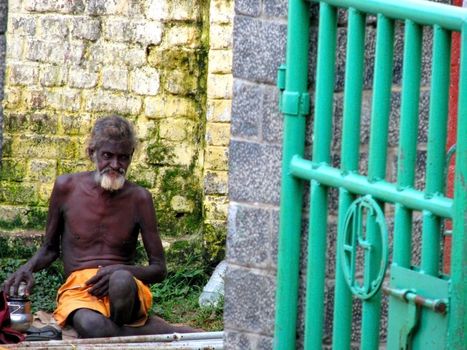 An elderly man in India waits at a gate entry.