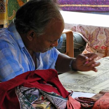An elderly artist in India creates cloth artwork.