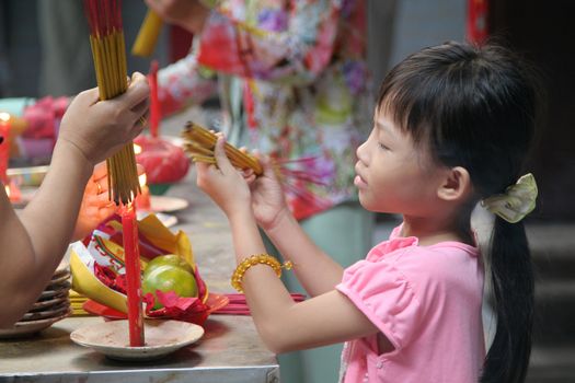 Young girl lighting a candle in a temple in Chinatown, Saigon