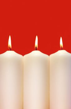 Three white holidays candles on a red background