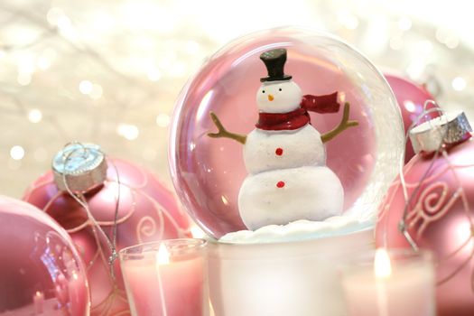 Snow globe with pink christmas balls and white lights in background
