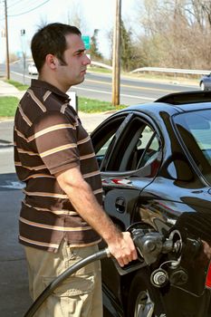 A man pumping high priced gas into his car with a disgusted look on his face.  