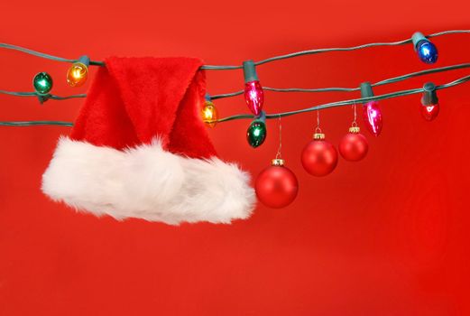 Hanging lights with santa hat and christmas balls against a red background