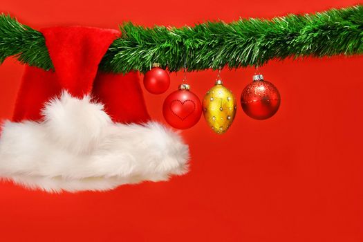 Green garland with santa hat and ornaments on red background