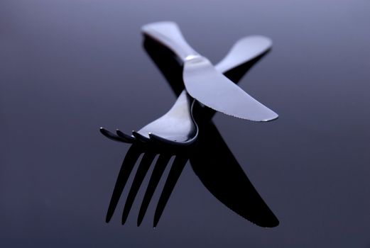 modern silver spoon, knife, fork on the mirror background