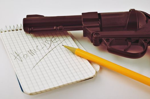 Close-up of a notepad with word 'homicide' written with pencil and gun with selective focus