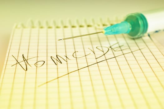 Close-up of a notepad with word 'homicide' written with pencil and syringe with very shallow depth of field