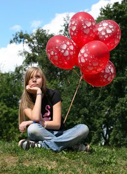The girl - teenager sits on a grass with red balloons