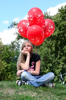 The girl - teenager sits on a grass with red balloons