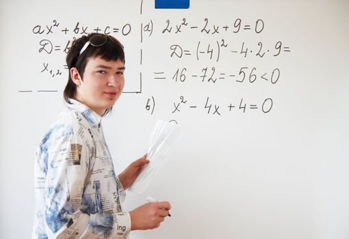 Young teacher teaching algerbra  and writes quadratic equation on a whiteboard