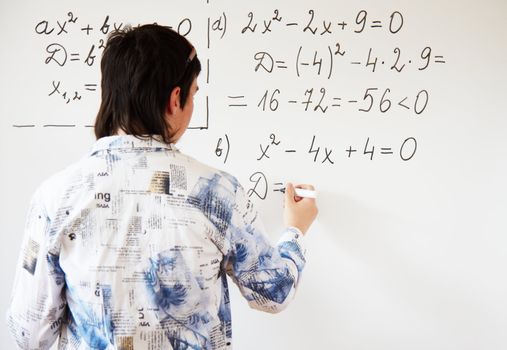 Young teacher teaching algerbra  and writes quadratic equation on a whiteboard