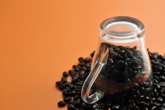 Transparent glass coffe cup up side down with coffe beans isolated on orange