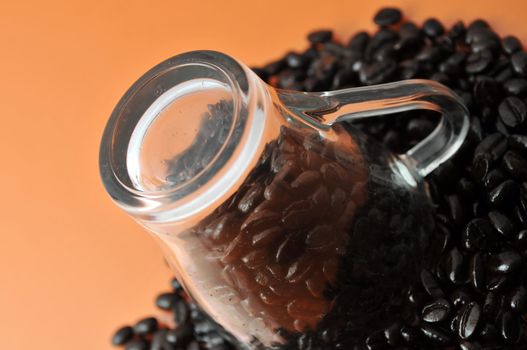 Transparent glass coffe cup up side down with coffe beans isolated on orange