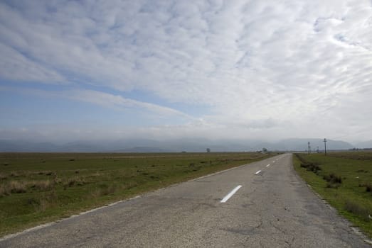 Sunny rural landscape with long straight road and blue cloudy sky