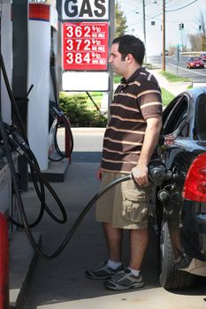 A man pumping high priced gas into his car with a disgusted look on his face.