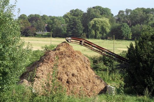 Huge manure heap and a rusty conveyor on a farm in Northern Germany, end of August.