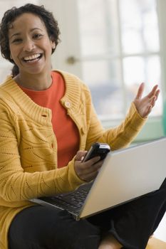 Beautiful young smiling African American woman using cell phone and laptop