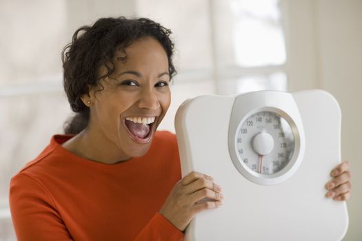 Beautiful young African American woman holding scale and shouting for joy