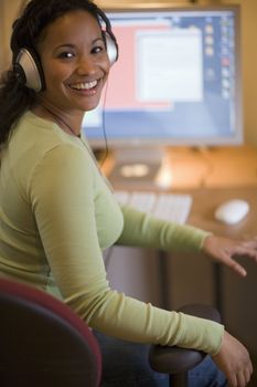 Smiling young African American woman with headphones at desk with computer
