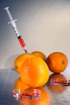 Syringe injecting liquid into an orange against dark background