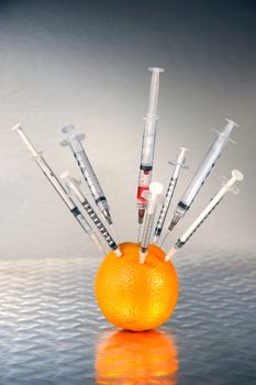 Syringes inserted into an orange against dark background