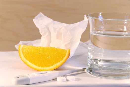Water glass with cold pills,tissue, thermometer and orange to fight flu symptoms