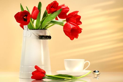 Red tulips in white container with tea cup
