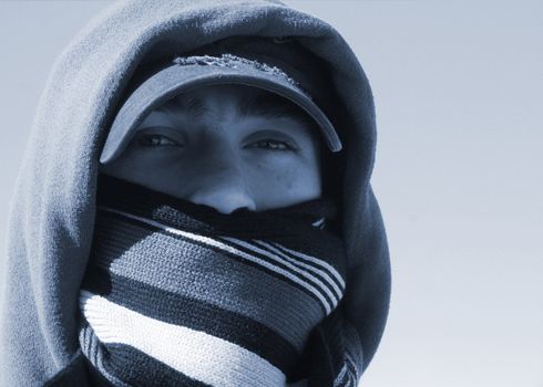 Duo-toned image of handsome young man with hat and knitted wool scarf covering his mouth on a cold winter day.